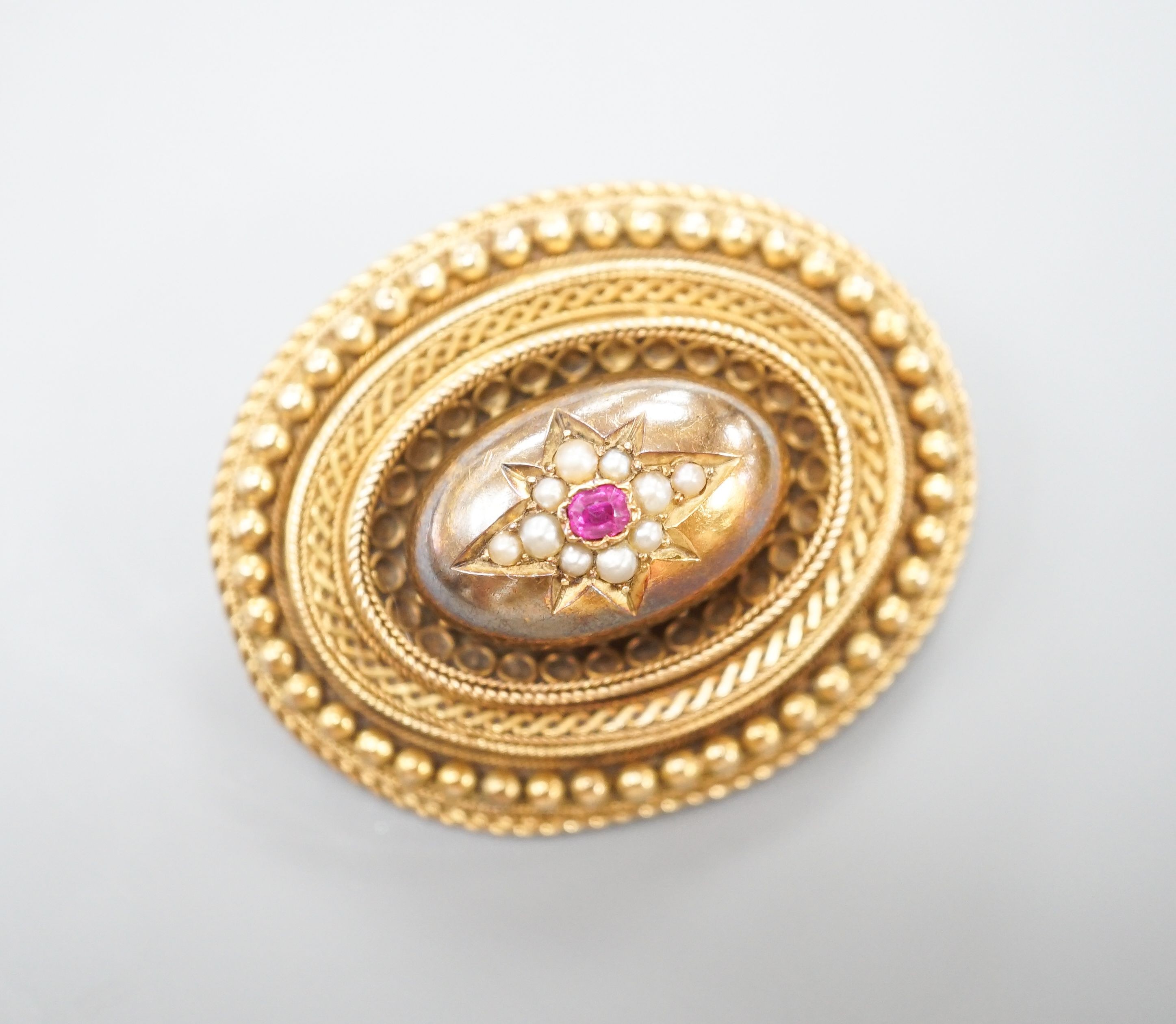 A Victorian yellow metal, ruby? and seed pearl set oval brooch, with glazed back, 43mm, gross weight 18.7 grams.